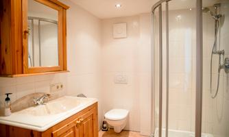 A modern bathroom with wooden cabinets and a shower. The walls are brightly tiled, and the room looks clean and inviting.