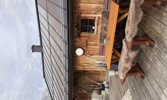 A cozy wooden cabin with a table and benches outside. The surroundings are rustic and inviting.