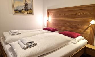 A cozy bedroom with two beds and red pillows. A beautiful landscape painting hangs on the wall.