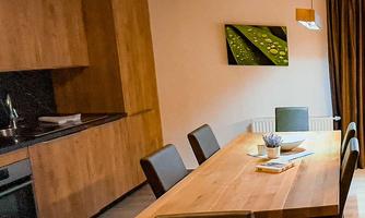 A modern dining area with a large wooden table and stylish chairs. The wooden kitchenette complements the inviting atmosphere.