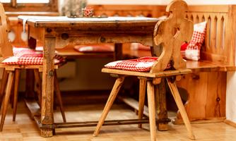 A rustic wooden dining table with a bench and two chairs. The seat cushions are red-and-white checkered and the surroundings exude a cozy atmosphere.