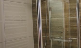 A modern shower cabin with glass walls and a wooden look. The walls are light tiled, creating a pleasant atmosphere.
