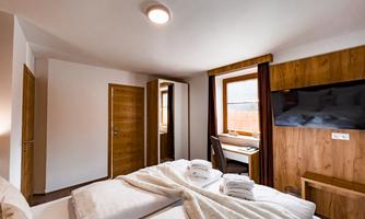 A modern bedroom with a double bed and a large window. There is a desk and a television on the wall.