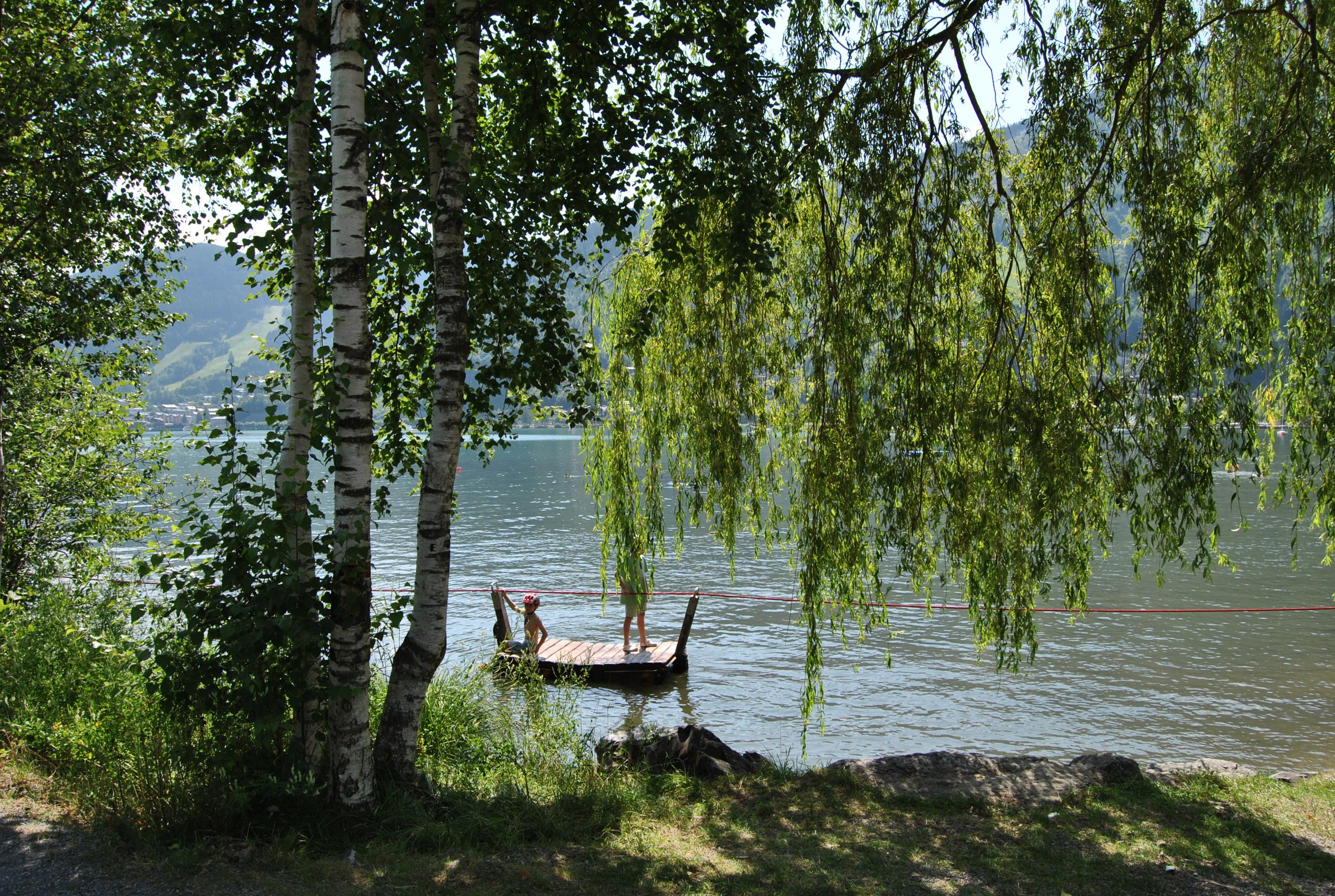 A tranquil lake with a floating wooden pier.  
Surrounded by green trees and gentle hills.