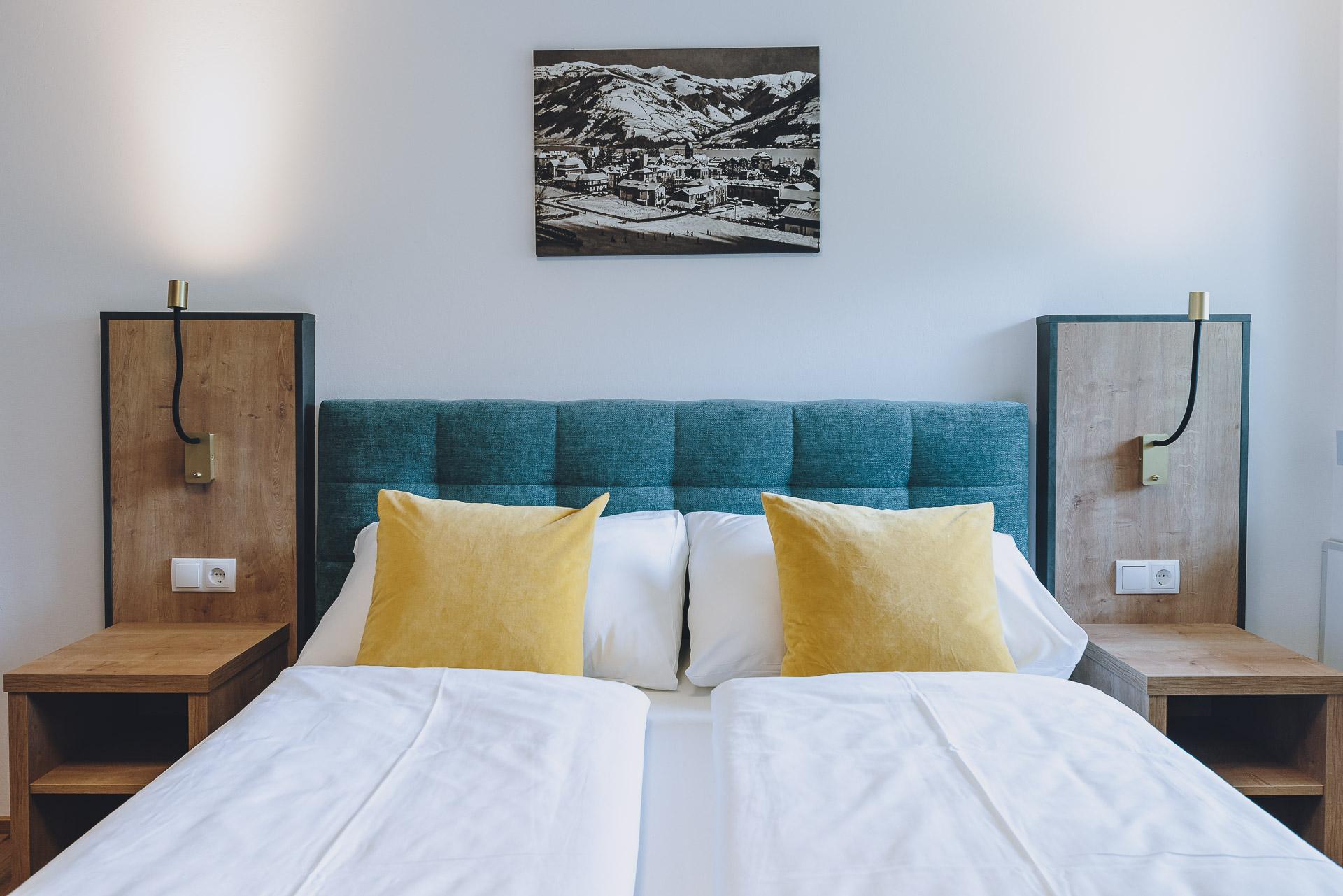 A modern bedroom with a comfortable bed and yellow cushions. Stylish bedside lamps and a framed picture are on the walls.