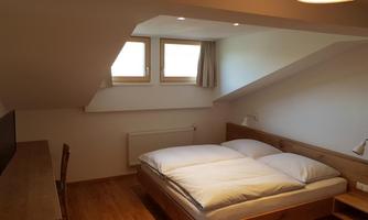 A cozy attic room with a double bed and two/windows. The room is bright and simply furnished with a wooden desk.