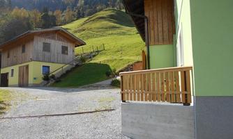 A peaceful rural scene with two houses and a green meadow in the background. The path between the houses gently leads into the hills.
