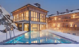 A modern building with large windows and a sparkling outdoor pool, surrounded by snow. The warm lighting creates an inviting atmosphere in the cold environment.