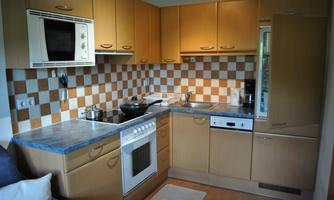 A modern kitchen with wooden cabinets and a blue countertop. The walls are decorated with a checkered tile design in various colors.