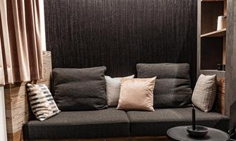 A modern living room with a cozy sofa and a small table. The walls are designed with wood and a dark fabric, creating a warm impression.