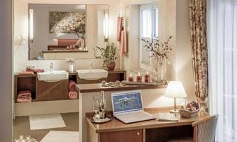 An elegant bathroom with two sinks and natural decor. Additionally, there is a workspace with a laptop and lighting.