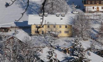 A snowy landscape with traditional houses and a yellow building in the center. The trees are covered with snow, and the sky is clear.