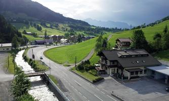 A picturesque landscape with green hills and a small river. In the foreground, there is a building, while mountains are visible in the background.