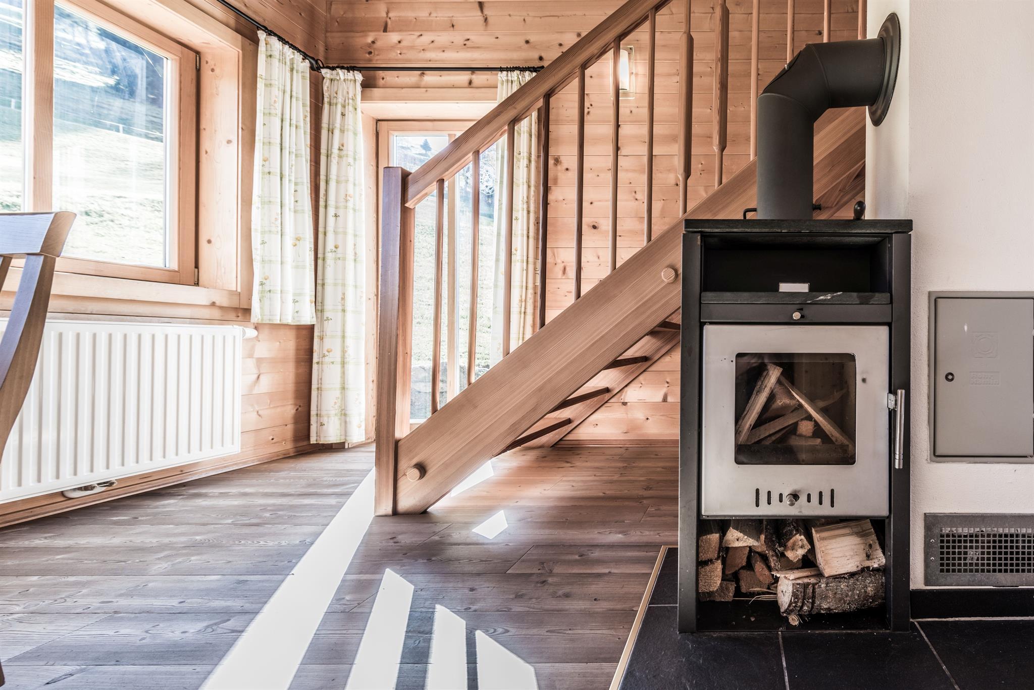 <p>A cozy room with a wooden floor, a fireplace and large windows. A staircase leads to the upper floor.</p>