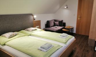 A cozy bedroom with two single beds and fresh, green bed covers. A seating area with a gray sofa and a small table complements the space.