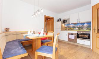 A modern kitchen with a wooden dining area and comfortable benches. The walls are bright and the furnishings are functional.