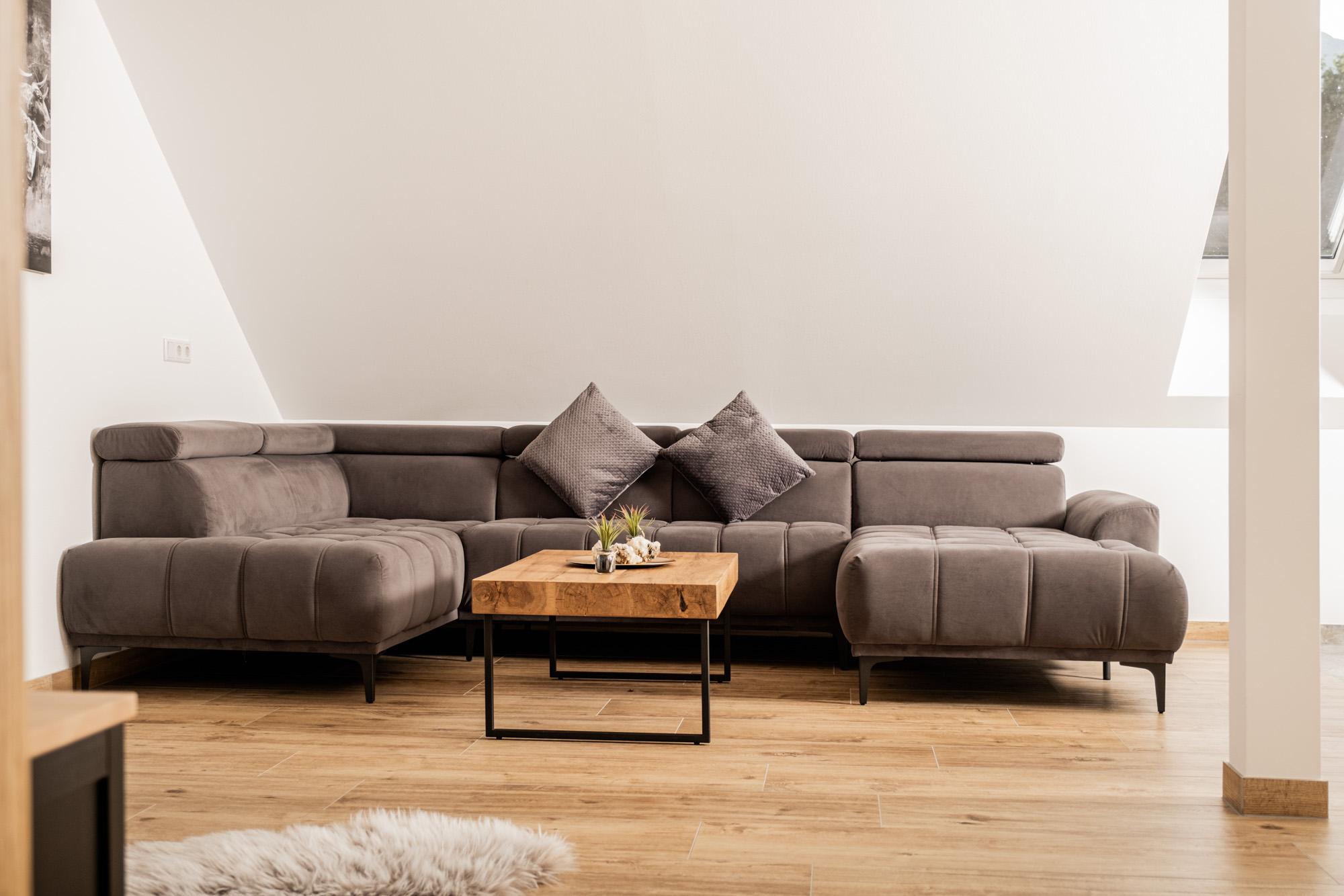 A modern living room with a gray sofa and a small wooden table. The room has light walls and wooden floors, creating a cozy atmosphere.