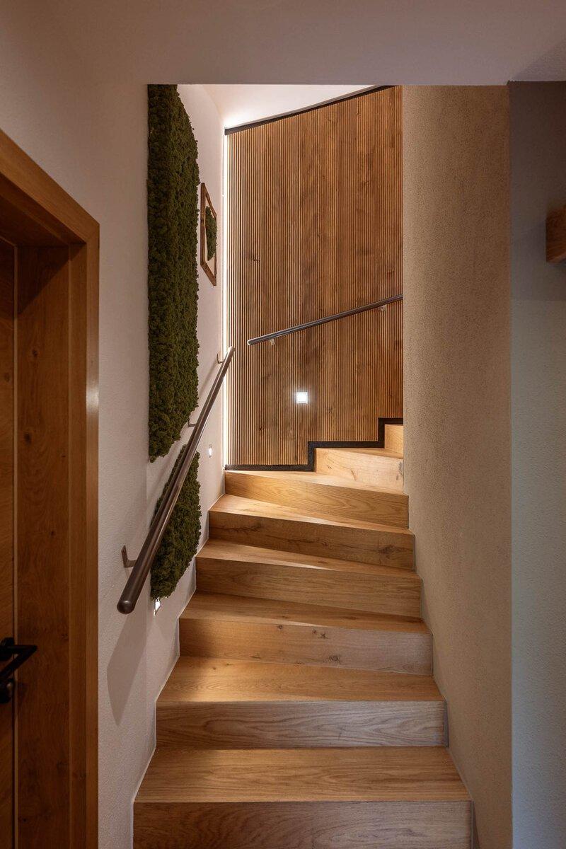A modern wooden staircase leads upwards. On the wall, green plants and pictures are decorated.