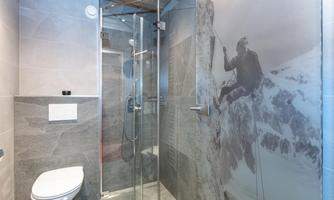 A modern bathroom with a glass shower cubicle and an elegant tiled wall. On the wall is a picture of a mountaineer in an alpine landscape.