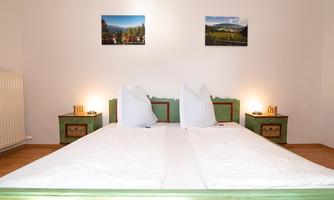 A stylish bedroom with a large bed and green nightstands. Pictures of mountain landscapes hang on the wall.