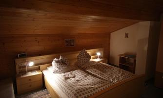 A cozy bedroom with wooden ceilings and a large double bed. Two nightstands with lamps and a small wardrobe complement the furnishings.