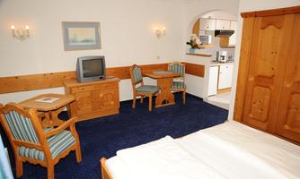 A cozy hotel room with wooden paneling and blue carpet. There is a table, chairs, and a small kitchenette.