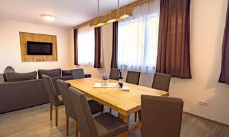 A modern dining area with a large wooden table and eight chairs. The windows let in plenty of natural light and the walls are painted in warm, neutral tones.