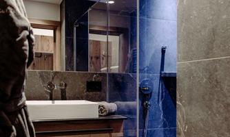 A modern bathroom with elegant tiles and a large shower. The sink is placed next to a wooden shelf with towels.