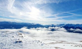 A beautiful winter landscape with snow-covered mountains and a bright blue sky. The sun shines above the clouds and offers a breathtaking view.