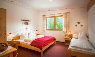 A cozy bedroom with two beds and a pleasant wooden decor. The room has a window overlooking greenery and decorative elements on the walls.