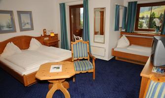 A cozy hotel room with a double bed and an additional single bed. The decor is made of wood with blue curtains and a small table.