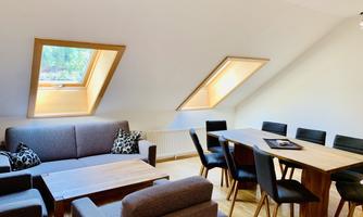A modern living room with comfortable sofas and a wooden table. Large skylights provide plenty of daylight.