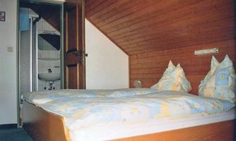 A simple room with a double bed and wooden paneling. In the background, a bathroom with a door is visible.