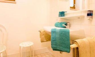 A modern bathroom with a white sink and colorful towels. The room is bright and friendly with a small stool and a large mirror.