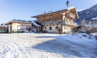 A cozy wooden house in winter with a snow-covered ground. In the background, snow-covered mountains can be seen.
