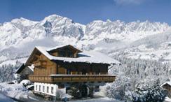 A charming wooden house in the snowy landscape. Majestic mountains rise in the background under the blue sky.