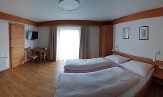 A cozy bedroom with two single beds and wooden wardrobes. The room is bright and well-furnished, with a view of a balcony.