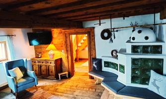 A cozy room with wooden ceilings and a tiled stove. There are comfortable armchairs, a TV, and a nice carpet.