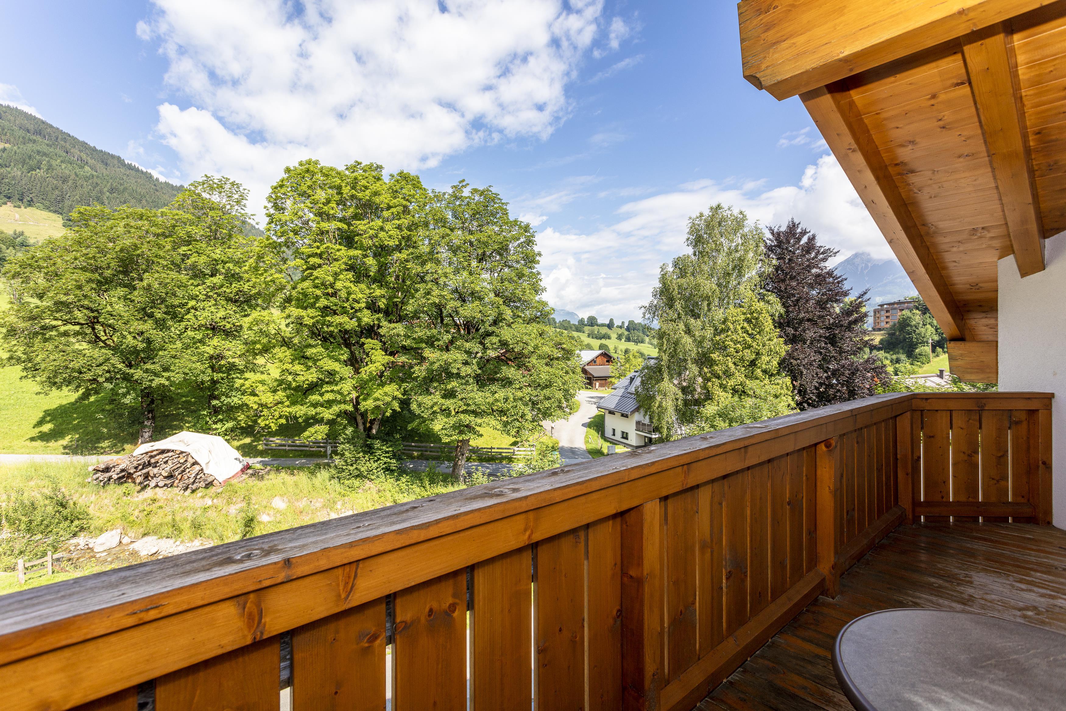 A beautiful view from a balcony overlooking a green landscape with large trees. The clouds in the blue sky give the scene a tranquil atmosphere.