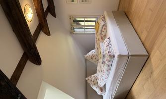 A cozy bedroom with a large bed and colorful pillows. The room has wooden beams and a window with a view outside.