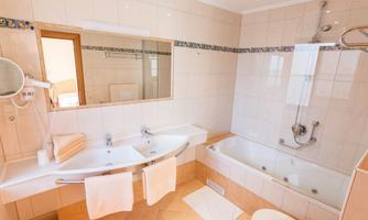 A modern bathroom with double sinks and a bathtub. Bright tiles and ample space create a pleasant atmosphere.
