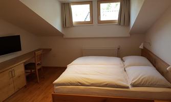 A cozy bedroom with a double bed and a small desk. The large windows let in plenty of daylight.