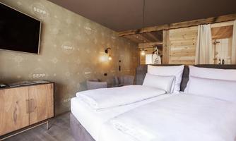A modern hotel room with a double bed and a cozy seating area. The walls are tastefully decorated and a television is mounted on the wall.