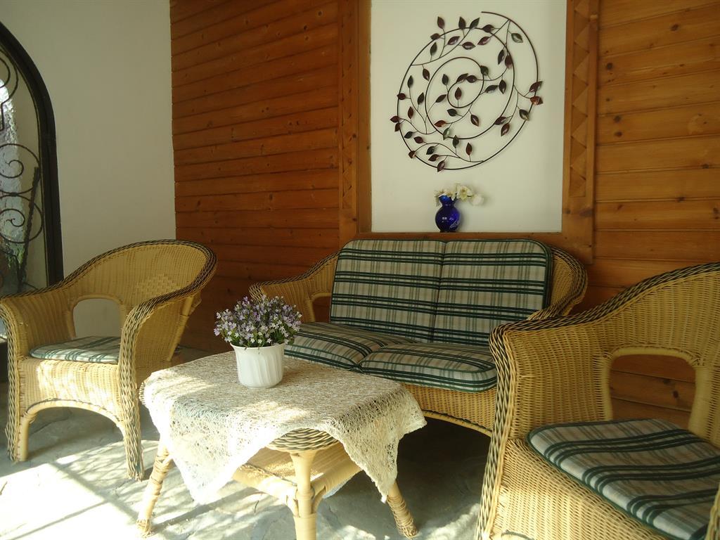 A cozy seating area with a rattan sofa and two chairs. A flower vase sits on the table and the room has warm wooden paneling.