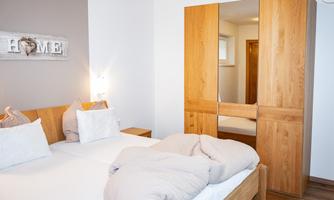 A modern bedroom with two beds, a wooden wardrobe, and neutral colors. The surroundings convey a cozy and inviting atmosphere.