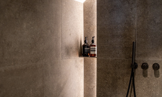 A modern shower with smooth gray tiles. On a small shelf corner, there are two bottles.