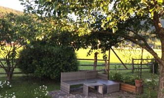 A cozy sitting area in the garden under a tree. In the background, green meadows and a fence can be seen.