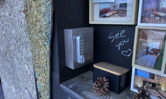 A modern key safe with a keypad on a wall. Next to it are a black box and two pine cones.