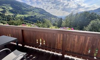 A beautiful balcony overlooking green mountains and a blooming landscape. The sun is shining and the sky is partly cloudy.
