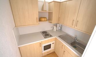 A modern kitchen with wooden cabinets and bright colors. It features cooktops, a sink, and basic kitchen appliances.